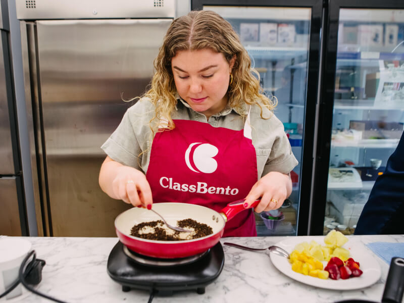 A woman in a ClassBento apron cooks food in a frying pan